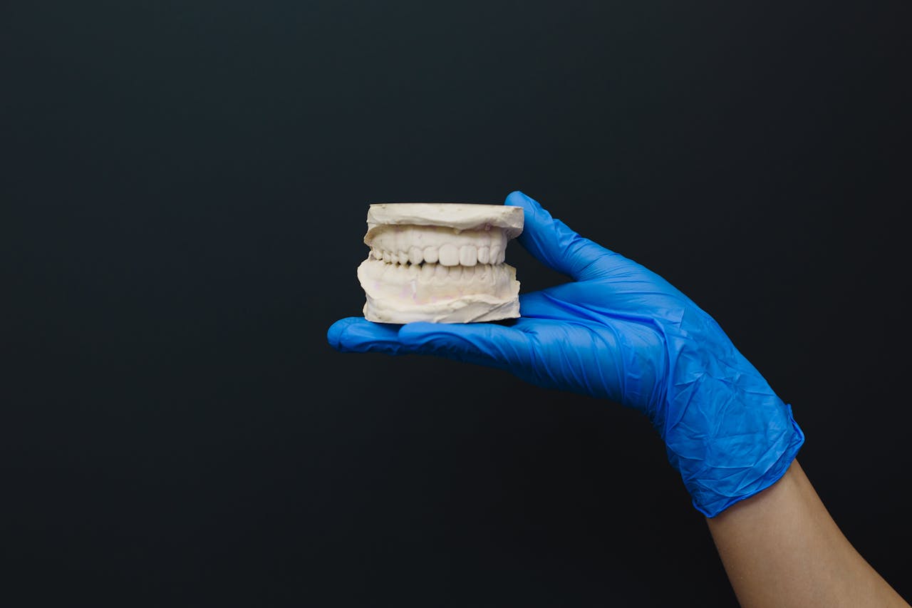 Close-up of latex-gloved hand holding dental model against a dark background.